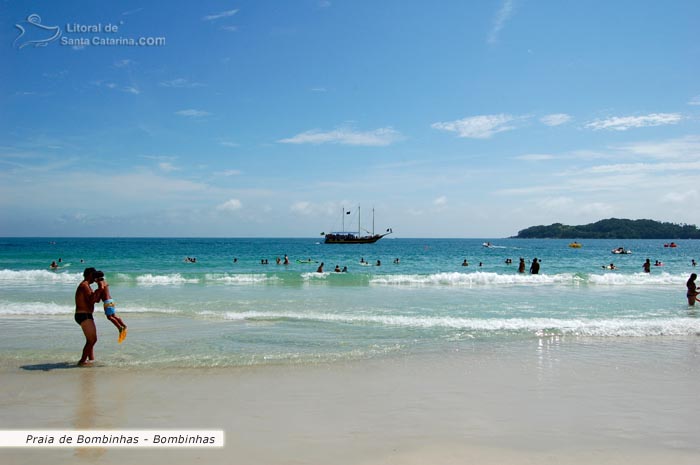 Pai brincando com seu filho e ao fundo o barco pirata passeando calmamente pela orla da Praia de Bombinhas.