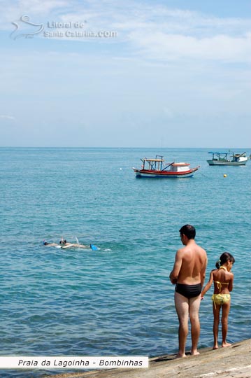 Pai e Filha olhando a limpeza do mar e ao fundo pessoas mergulhando na Praia da Lagoinha em Bombinhas.