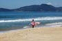 gata indo surfar e ao fundo a galera pegando umas ondas na praia e assim fazendo um surf neste dia maravilhoso