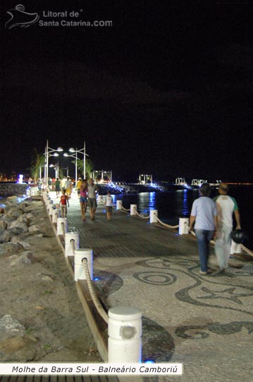 Pessoas caminhando pelo molhe da barra sul em Balneário Camboriú a noite.