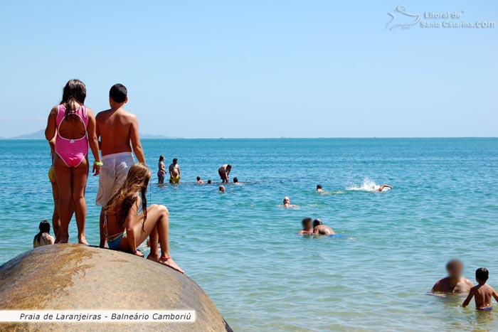 Crianças em cima da pedra e outras se divertindo no mar da praia de laranjeiras em balneário camboriú.