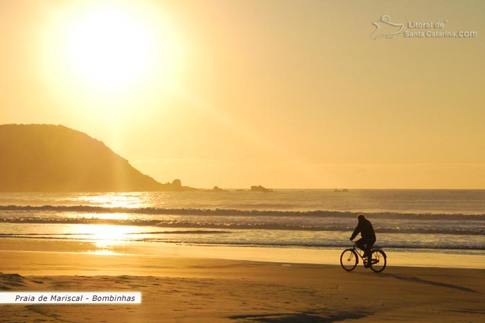 Nascer do sol na Praia de Mariscal  em Bombinhas e um senhor passeando calmamente de bicicleta pela praia, contemplando a natureza.