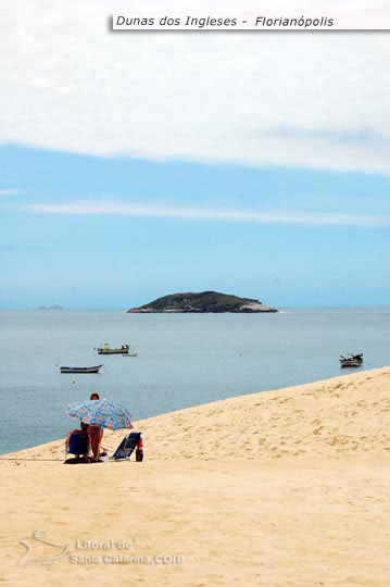 Pessoa tomando sol nas dunas dos ingleses e ao fundo um mar paradisíaco de santa catarina