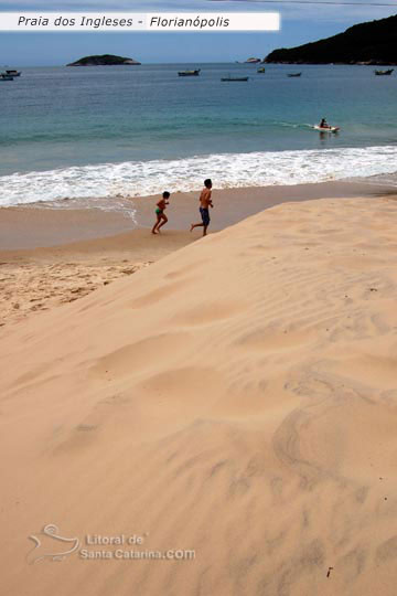 Pai e filhos correndo na praia dos ingleses e ao fundo uma pessoa andando de caiaque