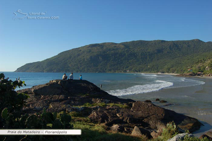 pessoas adimirando a beleza da praia do matadeiro em florianopolis, de cima da pedra