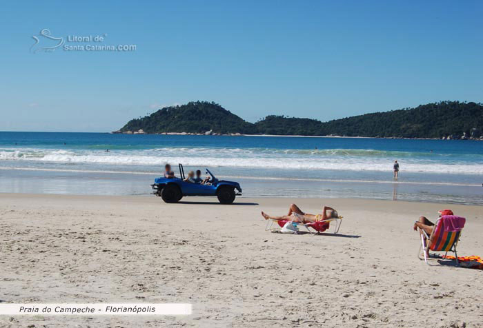 Bugui na praia do campeche em floripa, pessoas dencansando a beira mar e ao fundo o mar azul e ilha do campeche