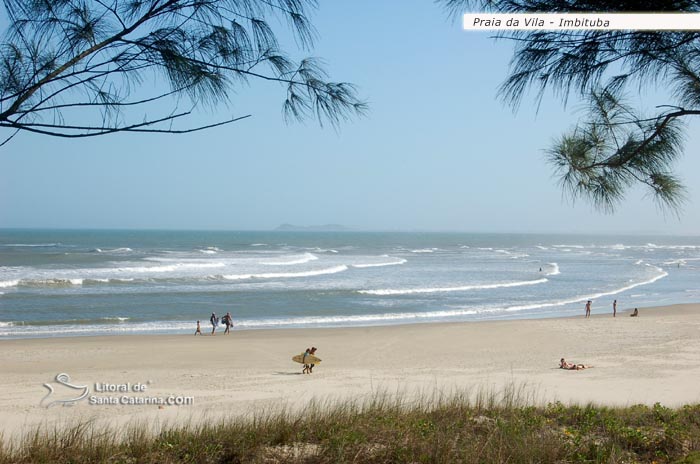 Uma galera indo para o surf, outra galera voltando e uma garota tomando sol na praia da vila