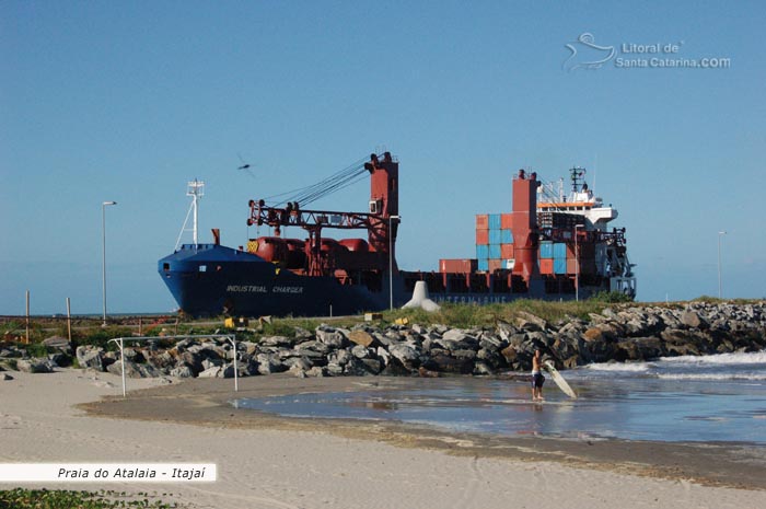 praia do atalaia, rapaz preparando sua prancha para ir surfar e ao fundo um navio cargueiro