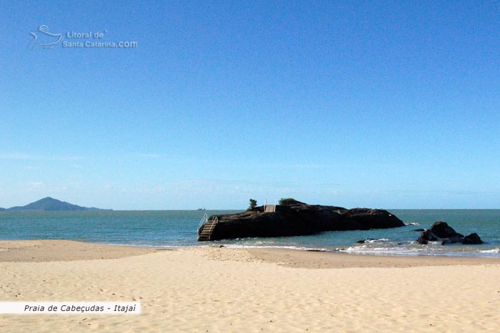 imagem linda da praia de cabeçudas, mar parecendo uma piscina e uma pedra ótima para pescar no meio deste cenário