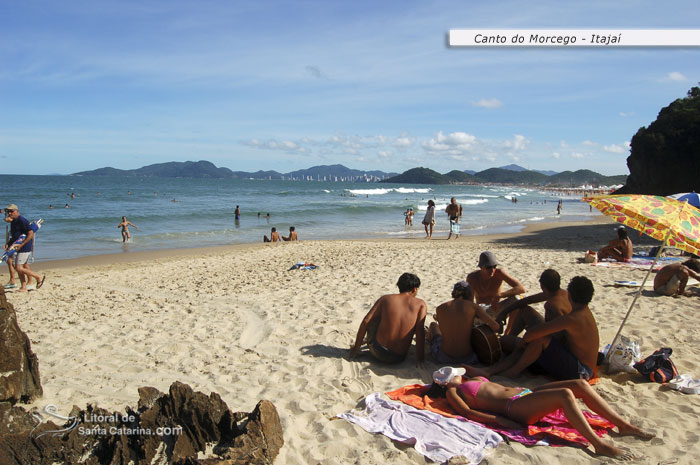 galera tocando um violão na praia do canto do morcego e outra nadando em suas águas límpidas