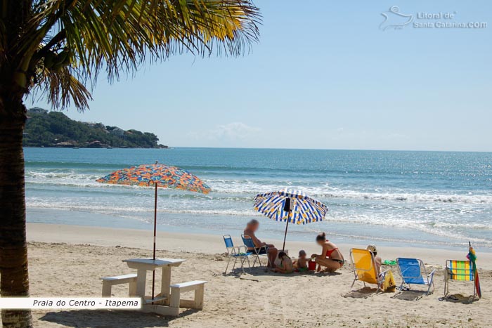 Mãe e filhos fazendo castelinhos com a areia da praia de itapema e ao fundo um mar lindo.