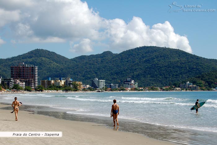 Praia de Itapema, pessoas caminhando calmamente e outras indo fazer um surf.