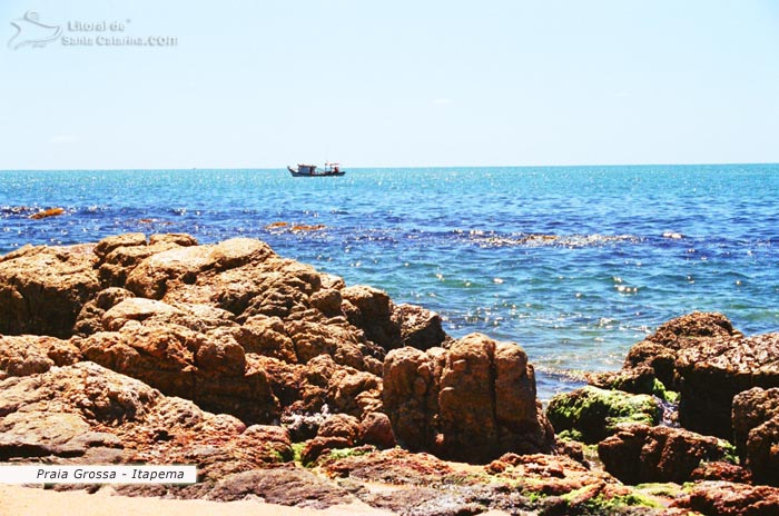 Praia Grossa, mar azul e um barco sozinho em busca de um peixe.
