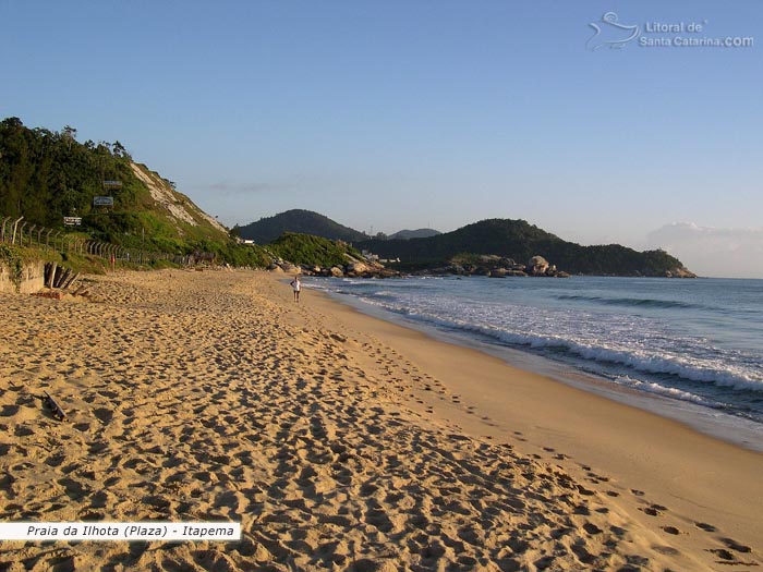 Pessoa fazendo caminhada nas areias da praia do plaza, morro lindo ao fundo e do lado um mar maravilhoso.