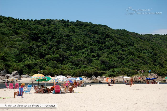 pessoas tomando sol e outras em baixo do guarda sol na praia da guarda