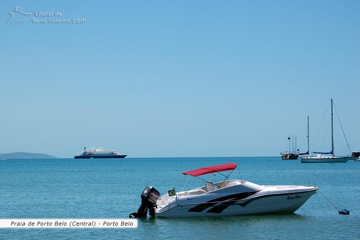 barco parado na praia central de porto belo e ao fundo um lindo navio transatlantico