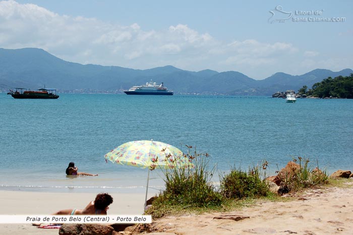 praia de porto belo, mulher tomando sol, crianças brincando na praia e ao fundo um lindo navio que veio fazer turismo em porto belo