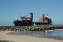 praia do atalaia, rapaz preparando sua prancha para ir surfar e ao fundo um navio cargueiro