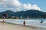 Praia de Itapema, pessoas caminhando calmamente e outras indo fazer um surf.