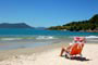 praia da pinheira, garota tomando sol e ao fundo um mar lindo e azul, pessoas se divertindo nas águas do litoral catarinense
